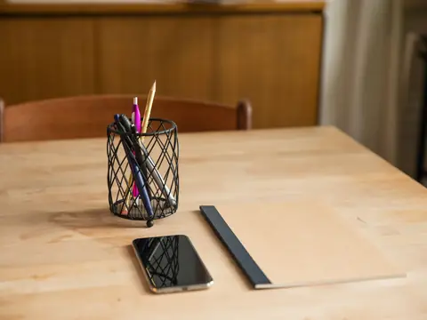 A phone and a pen pot on a wooden table