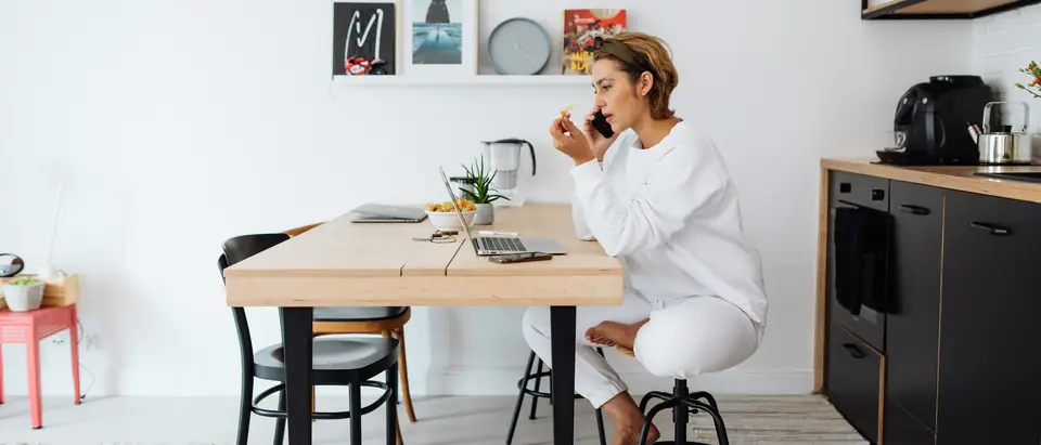 A woman on a phone call at a bright kitchen table