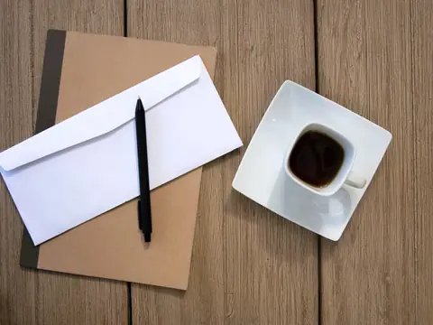 An envelope and a pen on a notebook beside a coffee cup