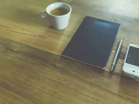 A notebook, a pen and a phone beside a cup of coffee