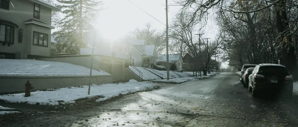 A slushy residential street with cars parked along it in winter