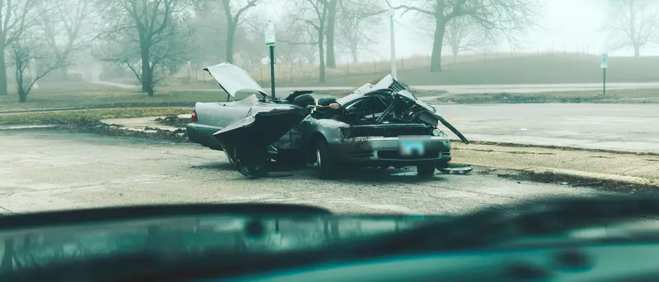 A wrecked car on a foggy park road, seen through a windshield