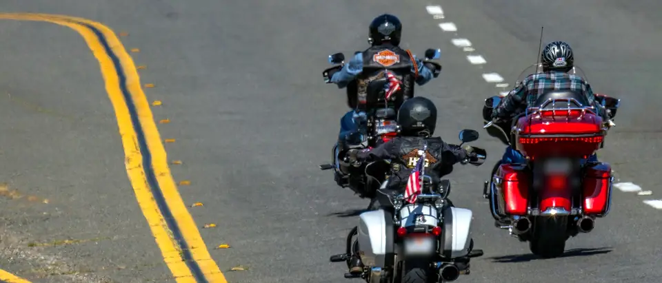 Three riders on touring motorcycles on a road with double yellow lines