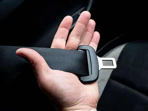 A hand holding a seat belt buckle inside a car