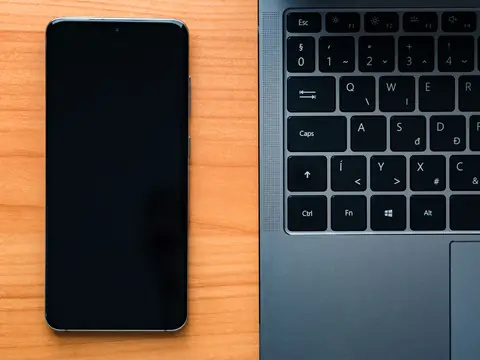 A phone beside a laptop keyboard on a wooden desk