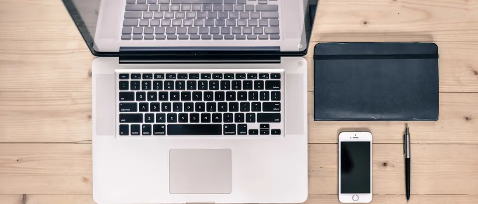 A laptop, a notebook, a phone and a pen on a wooden table