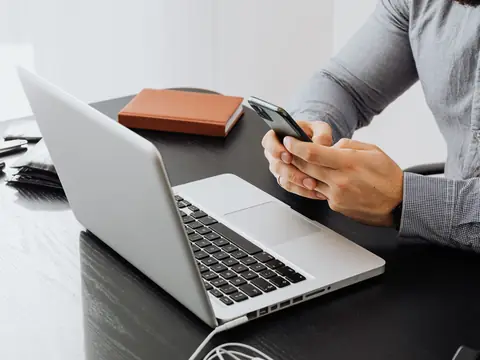 A man holding a phone at a laptop