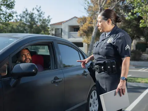 A police officer with a clipboard talking to a driver in a parked car
