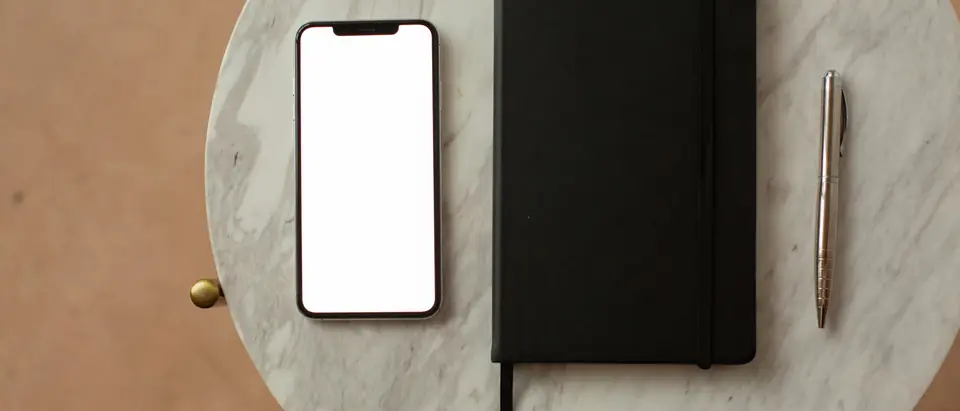 A phone, a notebook and a pen on a marble table