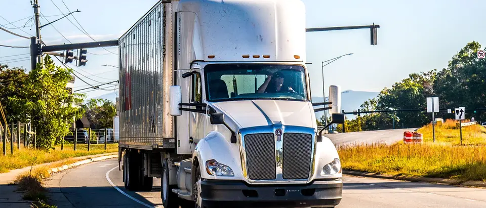 A white semi truck pulling a trailer through an intersection