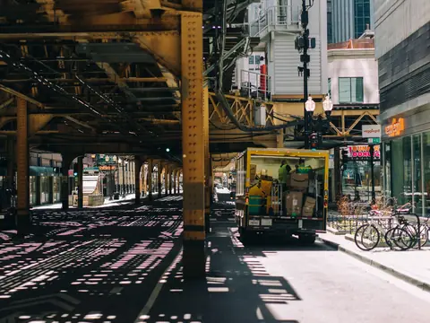 A delivery truck parked under an elevated rail line