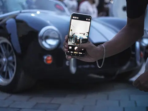 A hand holding up a phone to photograph a car